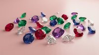 Collection of colorful precious gemstones including diamonds, rubies, emeralds and sapphires scattered on pink surface for luxury jewelry design.