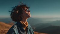 Young woman with curly hair enjoying freedom on mountain peak during golden hour sunset with scenic landscape background for adventure travel concepts.