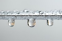 Water droplets hanging from wet surface with crystal clear reflections on neutral background for freshness and purity concepts.