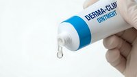 Derma clinic ointment tube being squeezed, dispensing clear gel drop from nozzle. Hand holding medical skincare product for treatment and healing applications.