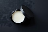 Open black cosmetic compact with cream concealer or foundation on dark background for makeup and beauty applications.