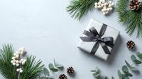 Christmas gift box with black ribbon surrounded by pine branches, white berries and pinecones on light background for holiday greeting cards.