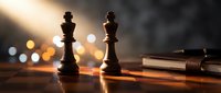 Chess king and queen pieces on wooden board with warm bokeh lighting and pen creating strategic business concept atmosphere.