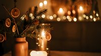 Festive arrangement with dried citrus slices and evergreen branches in copper vase, warm string lights creating bokeh background, seasonal holiday decoration for home styling and festive occasions.