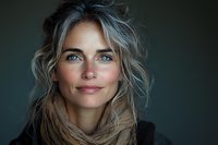 Close up portrait of young Caucasian woman with messy blonde hair and natural makeup wearing brown scarf, smiling against dark background. Soft lighting highlights facial features.