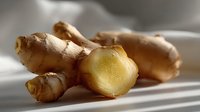 Fresh ginger root with cut piece showing yellow flesh interior on white fabric background with soft shadows, close up view for cooking and wellness.