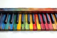 Colorful piano keys painted in rainbow colors against white background, artistic musical instrument close-up showing vibrant spectrum of hues on keyboard.