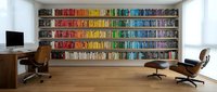 Modern home office with colorful rainbow bookshelf wall, wooden desk, ergonomic chairs and hardwood floors for contemporary interior design inspiration.