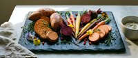 Assorted cured meats and sausages arranged on slate board with fresh vegetables and garnish for charcuterie board presentation.