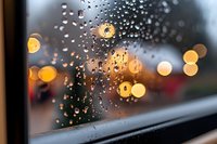 Raindrops on window glass with blurred golden bokeh lights creating atmospheric mood. Water droplets catch evening city illumination in soft focus.