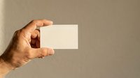 Hand holding blank white business card against neutral beige background, ready for custom branding and design mockups for corporate identity projects.