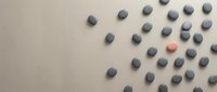 Gray pills scattered on beige surface with one orange capsule standing out among medication tablets for healthcare and pharmaceutical concepts.