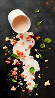 Spilled milk with scattered pink flower petals and fresh mint leaves creating artistic composition on dark background. Food photography for restaurant menus.