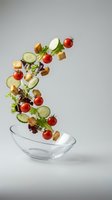 Fresh salad ingredients falling into glass bowl with cherry tomatoes, cucumber slices, lettuce leaves and croutons on neutral background.