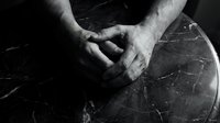 Male hands clasped together in prayer or meditation pose on dark marble surface, black and white artistic photography for spiritual wellness concepts.