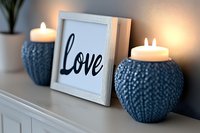 Cozy home decor with white framed love sign and two blue knitted ceramic candle holders with glowing tea lights creating warm atmospheric lighting.