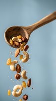 Mixed nuts and raisins spilling from wooden spoon on blue background. Healthy snacking, trail mix ingredients cascading with motion blur effect.