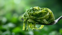 Fresh pasta with vibrant green pesto sauce twirled on a fork against blurred natural background, showcasing Italian cuisine in appetizing detail.