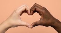 Two diverse hands forming heart shape symbol representing unity love and friendship on peach background for social campaigns and diversity projects.