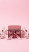 Pink velvet gift box with satin bow surrounded by cherry blossoms on pastel pink background, spring celebration concept.