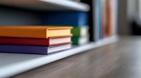 Colorful hardcover books stacked on white shelf against dark wooden table surface with soft blur effect creating minimalist study atmosphere.