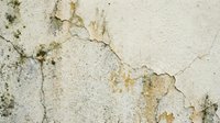 Weathered concrete wall with peeling paint, cracks, and rust stains showing natural aging and decay texture for industrial or grunge design backgrounds.