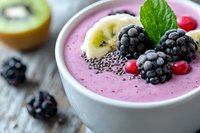 Pink berry smoothie bowl topped with fresh blackberries, banana slices, kiwi, chia seeds and mint leaves on rustic wooden background. Healthy breakfast concept.
