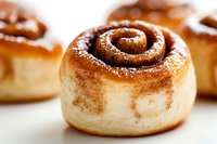 Fresh baked cinnamon roll with swirled spice filling and powdered sugar dusting on white surface, extreme close up showing soft dough texture and golden brown color.