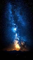 Vibrant Milky Way galaxy stretching across night sky with glowing blue and golden colors above dark mountain silhouette, stars scattered across space.