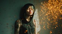 Young Asian woman with closed eyes in dark clothing against teal wall, illuminated by golden sparks and light flares creating dramatic atmospheric portrait.