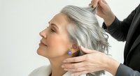 Senior woman with gray hair receiving neck and shoulder massage from therapist in black uniform against white background. Wellness treatment.