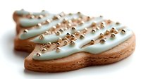 Festive sugar cookie shaped as Christmas tree decorated with mint green frosting and golden sprinkles on white background, macro food photography.