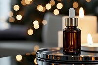 Brown glass dropper bottle with essential oil on metallic tray against blurred warm bokeh lights and glowing candles, creating spa atmosphere.