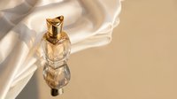 Luxury fragrance bottle with golden atomizer on beige background with flowing silk fabric and soft shadows, suitable for perfume marketing and beauty product advertising.