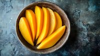 Fresh sliced mango in rustic ceramic bowl on textured blue background, vibrant tropical fruit for healthy eating and food photography.