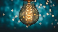 Vintage Edison bulb with spiral filament glowing warmly against blurred blue bokeh lights background for creative lighting and electrical concepts.