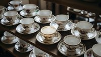 Elegant vintage porcelain tea cups and saucers with floral patterns arranged on wooden shelves in antique shop or kitchen display for dining decor.