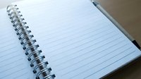 Open spiral notebook with blank lined pages and a pen, ready for notes, journaling, or planning on a wooden desk surface.