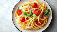 Delicious spaghetti pasta with fresh cherry tomatoes and basil leaves on white plate, traditional Italian cuisine served on light background.