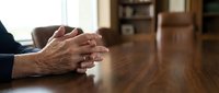 Businessman hands clasped on wooden conference table in modern office boardroom during corporate meeting or negotiation session.