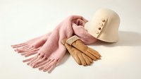 Stylish winter accessories set with pink knitted scarf, cream wool hat and brown leather gloves arranged on neutral background for fashion styling.