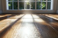 Sunlight streaming through window creates dramatic shadows on polished hardwood flooring, highlighting natural wood grain texture and warm tones in modern interior.