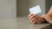 Male hands holding blank white credit card against neutral background for payment and financial services concepts.