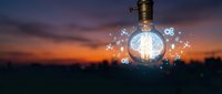 Glowing light bulb with digital icons floating around it against sunset cityscape backdrop, representing innovation, creativity, and smart business solutions.