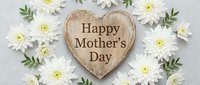 Wooden heart with Happy Mother's Day text surrounded by white daisies and green leaves on light background for greeting cards and celebrations.