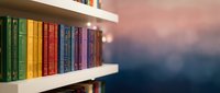 Colorful books arranged on white wooden shelves with warm bokeh lighting creating cozy reading atmosphere for home library interior design.
