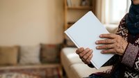 Senior woman with dark skin tone holding blank white tablet or document in living room setting, suitable for healthcare, education, technology, communication, and lifestyle concepts.