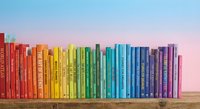 Colorful rainbow arrangement of books on wooden shelf against pastel sky background creating vibrant literary display for education and reading concepts.