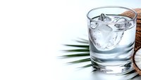 Glass of pure water with ice cubes, coconut and palm leaf on white background. Fresh tropical drink concept with copy space for text.