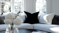 Elegant corner sofa with black and white cushions in sunlit living room featuring cotton stems in vase, arched windows casting natural light patterns.
